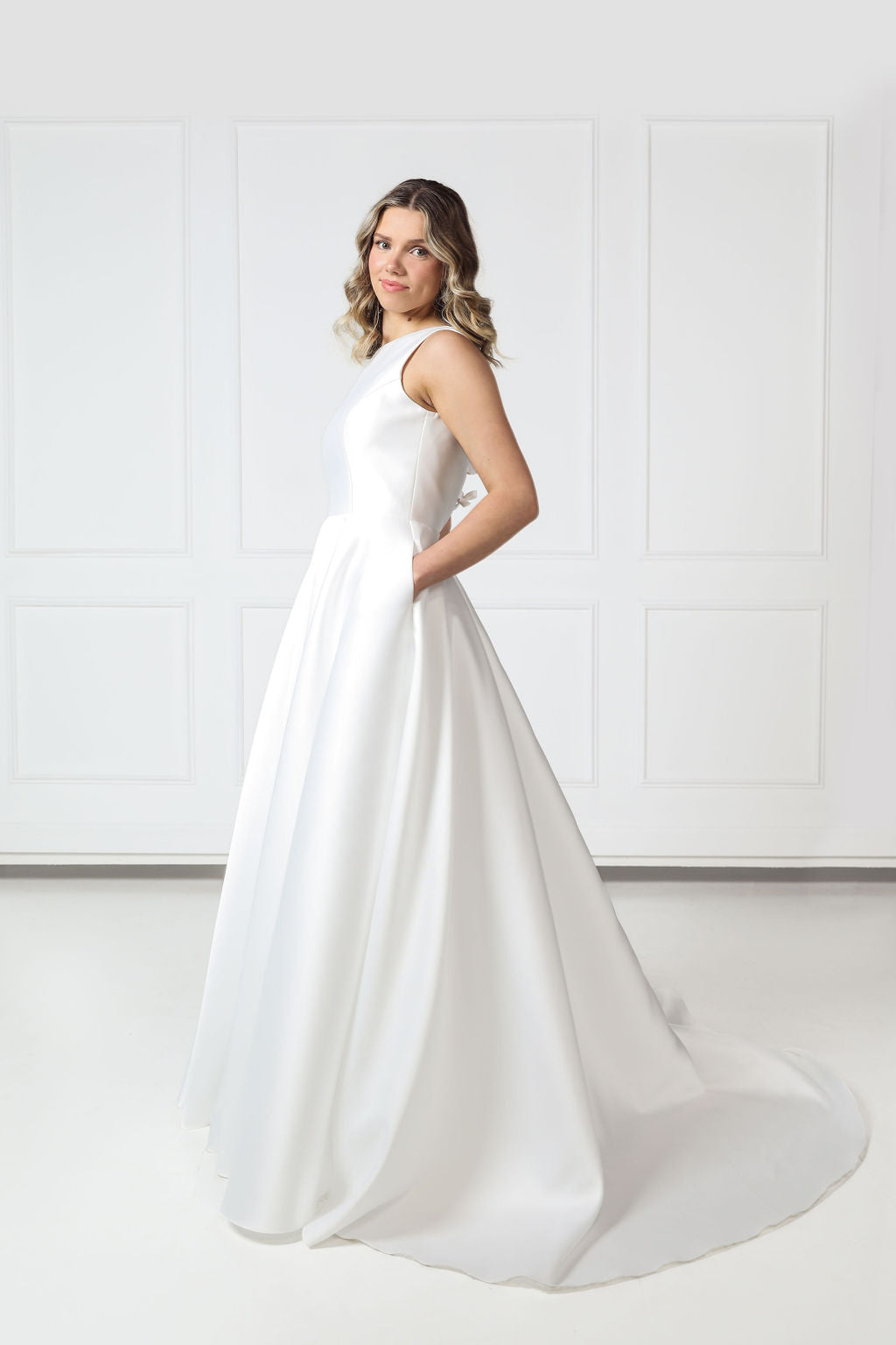 Side profile of boat-neck wedding gown showing the structured waist, flowing full skirt, and glossy Mikado finish.