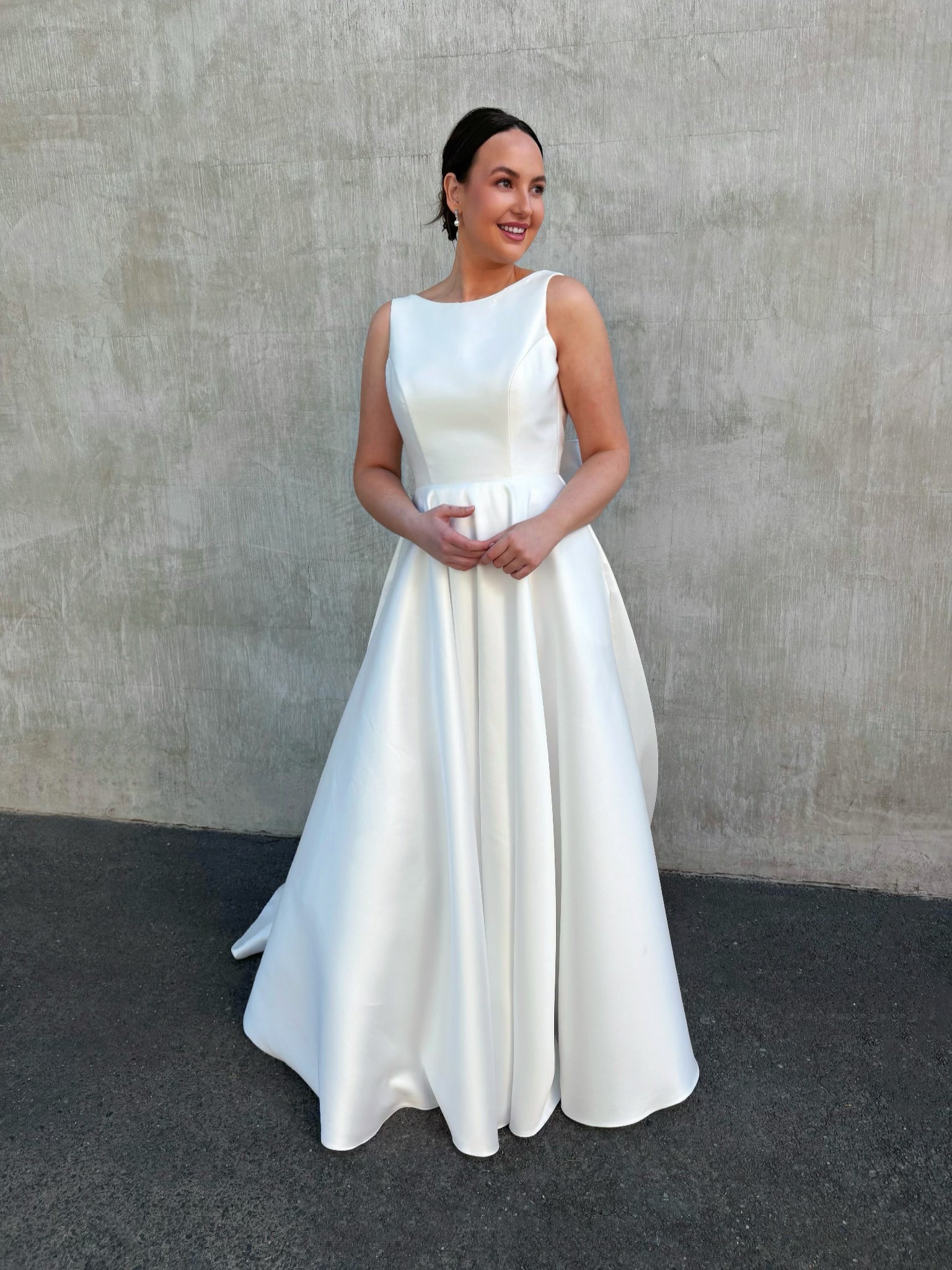 Front view of elegant boat-neck wedding dress in glossy satin Mikado with a cinched waist and full princess skirt