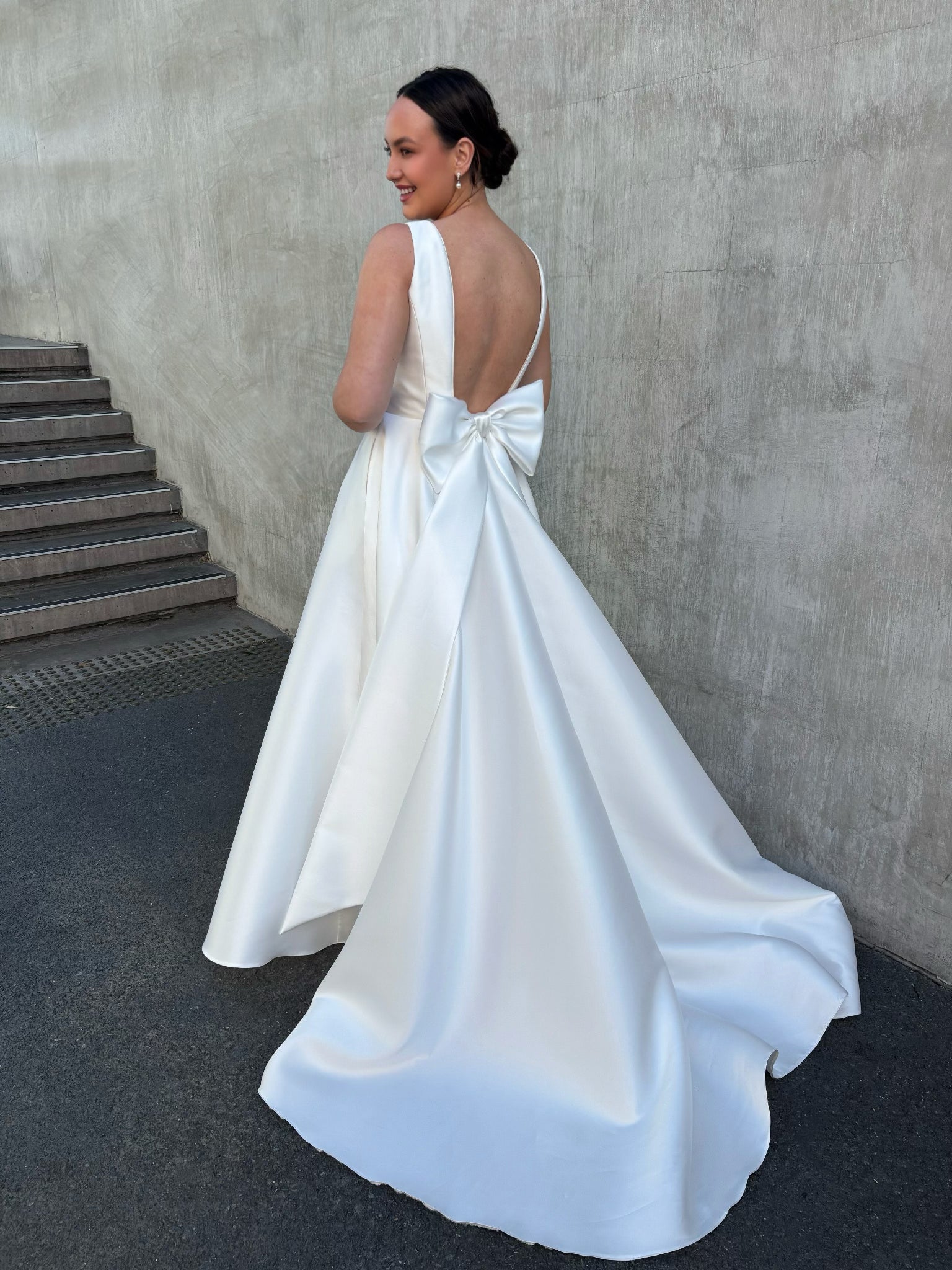 Back view of boat-neck bridal gown featuring optional oversized bow and low-back or backless design in satin Mikado.