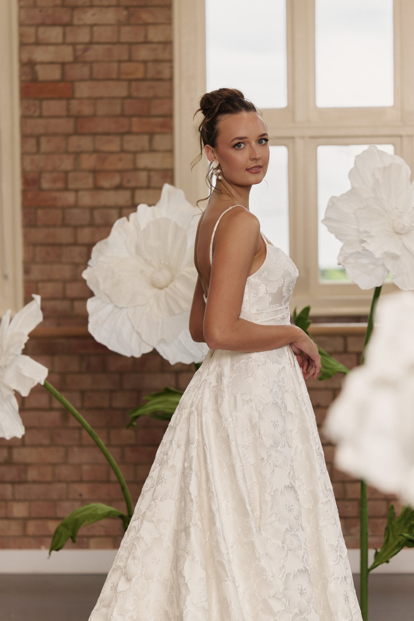 Bride wearing floral jacquard wedding dress with V-neck, spaghetti straps, structured bodice, and dramatic full circle skirt.