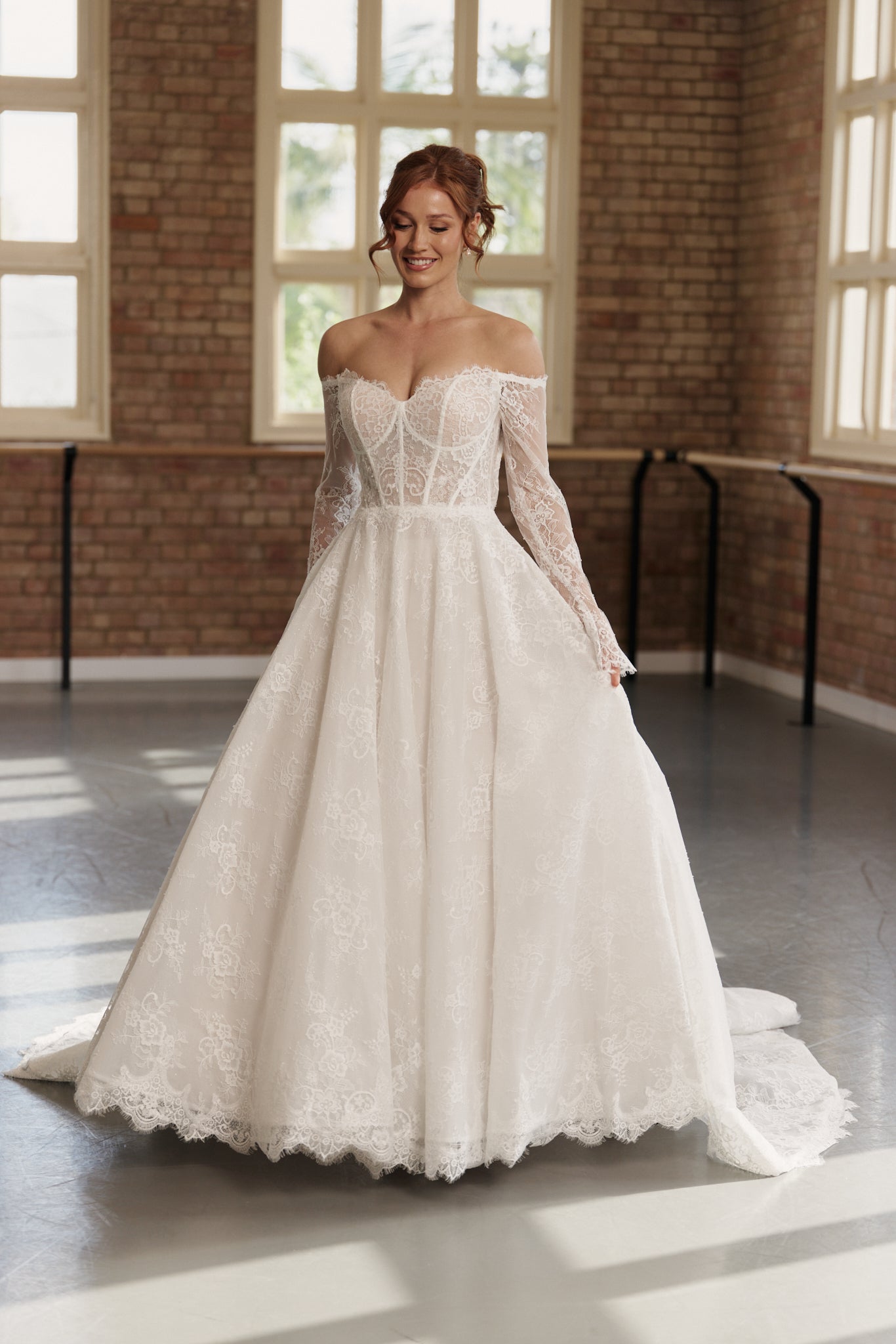 Bride wearing Elle wedding dress with off-shoulder long lace sleeves, corseted bodice, and princess-style lace skirt.