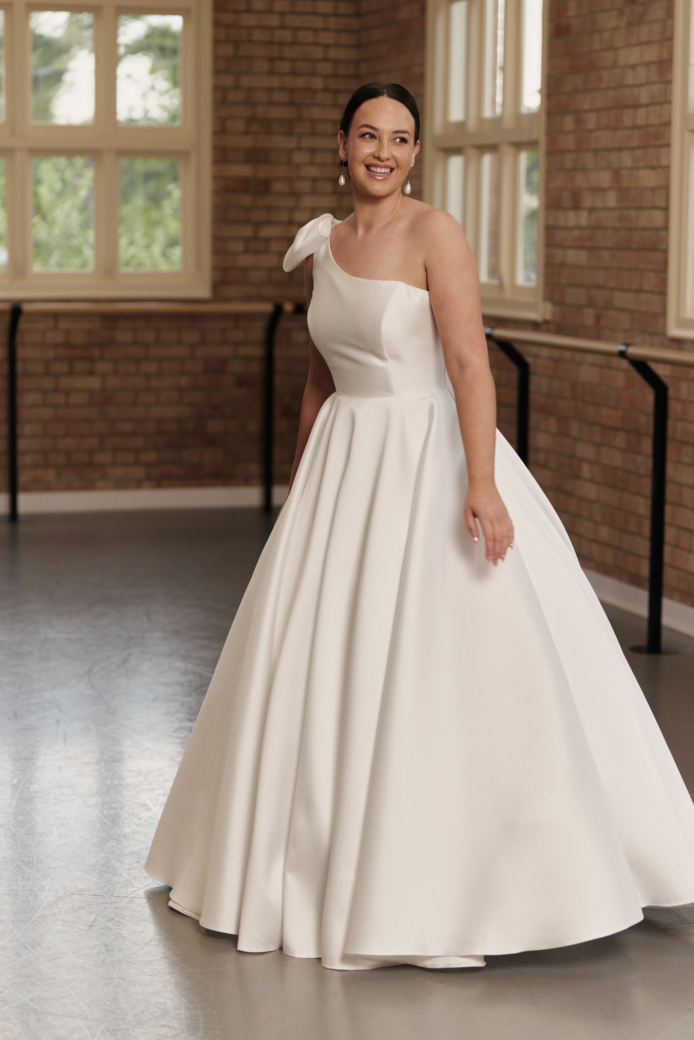 The Emily gown, asymmetric one-shoulder bridal dress with a bow, fitted bodice, and full satin skirt.