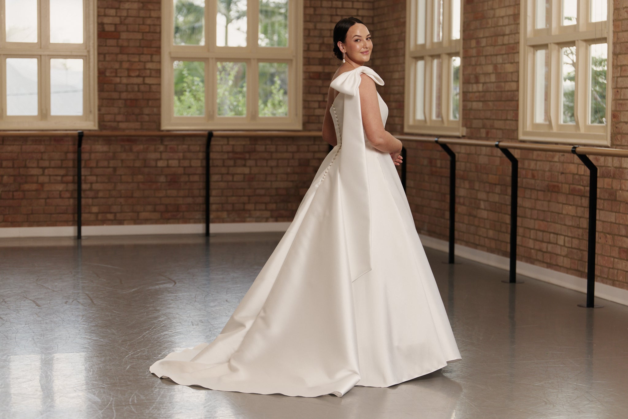 Side profile of the Emily gown highlighting the elegant one-shoulder bow, cinched waist, and voluminous Mikado skirt