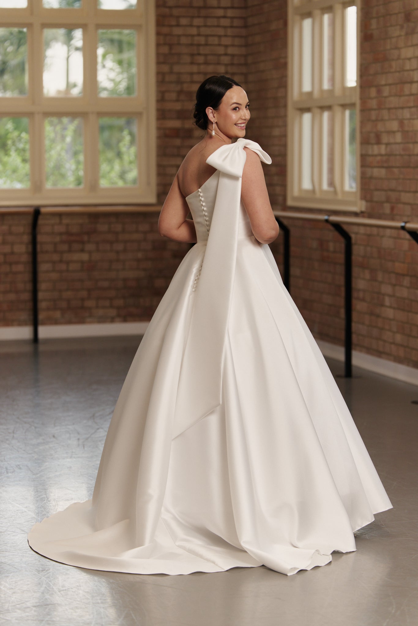 Back view of the Emily bridal gown showing the asymmetric one-shoulder design, button detail, structured waist, and optional train