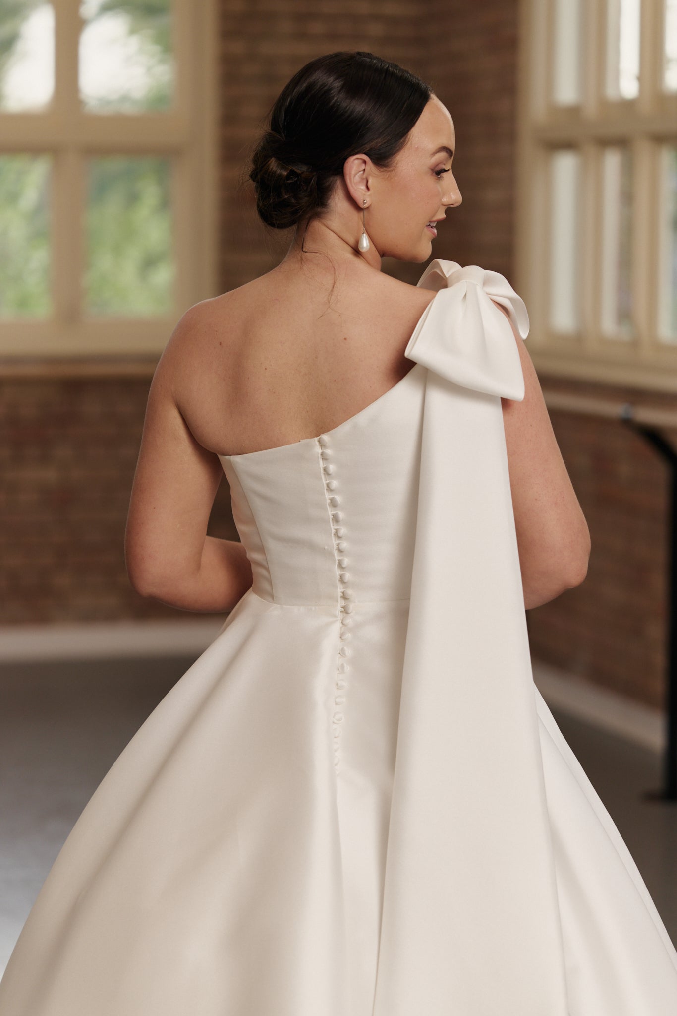 Close-up of the Emily gown’s one-shoulder bow and full button detail, crafted from glossy Mikado satin