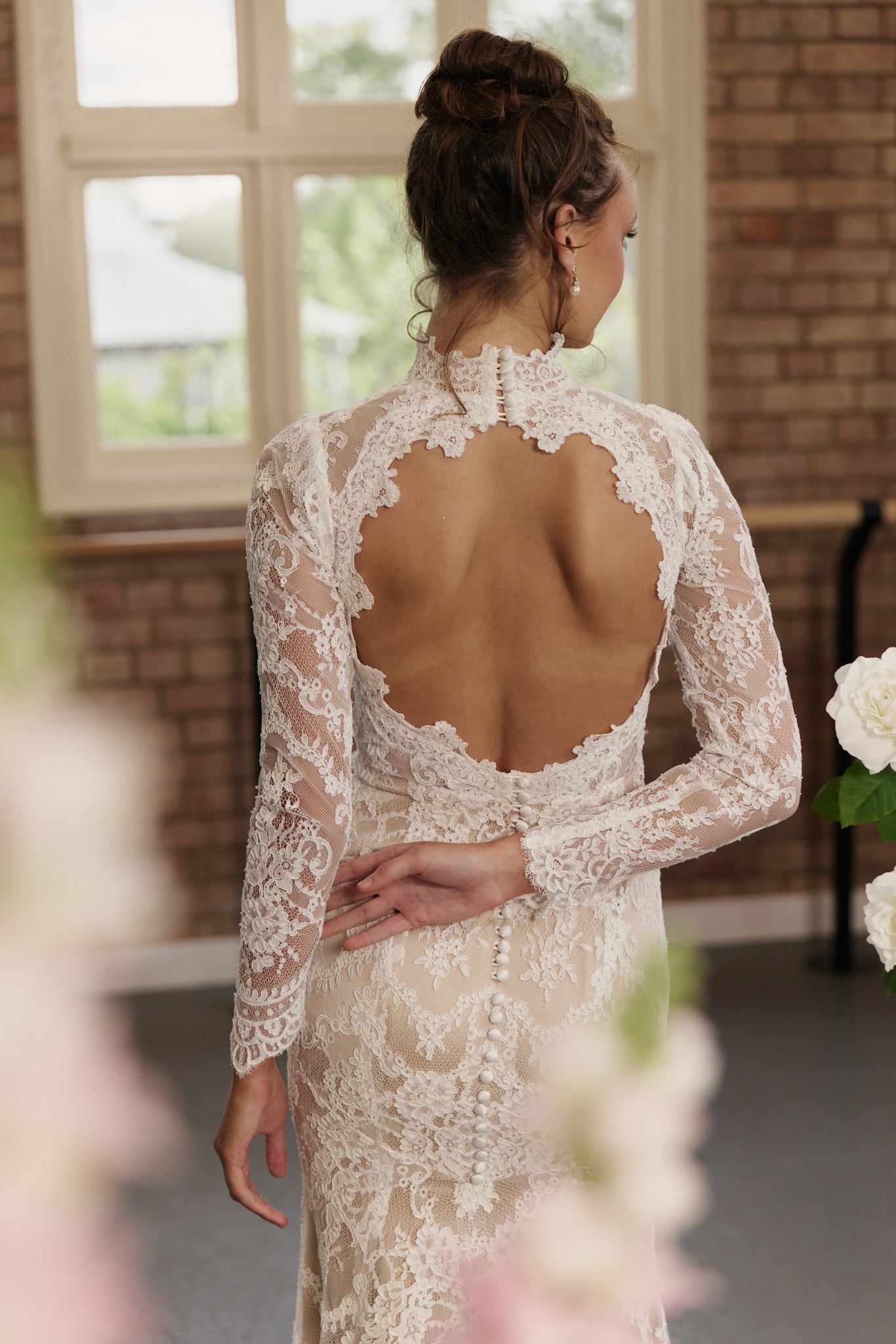 Close-up of the open back and lace detailing on the elegant sheath wedding dress with long sleeves.