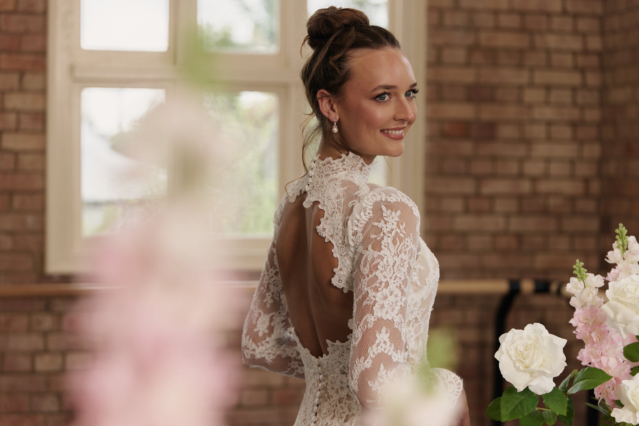 Side view of lace sheath wedding gown with high neckline, open back, and long sleeves.