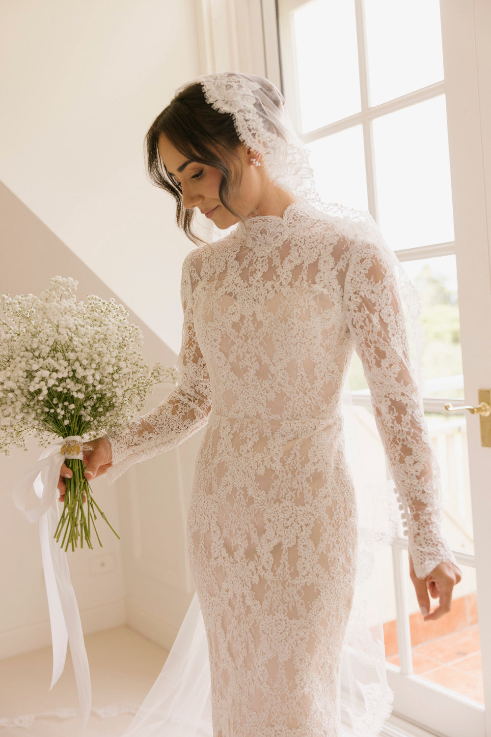 Jess wedding dress with long lace sleeves, high neckline, open back, and fitted silhouette with train