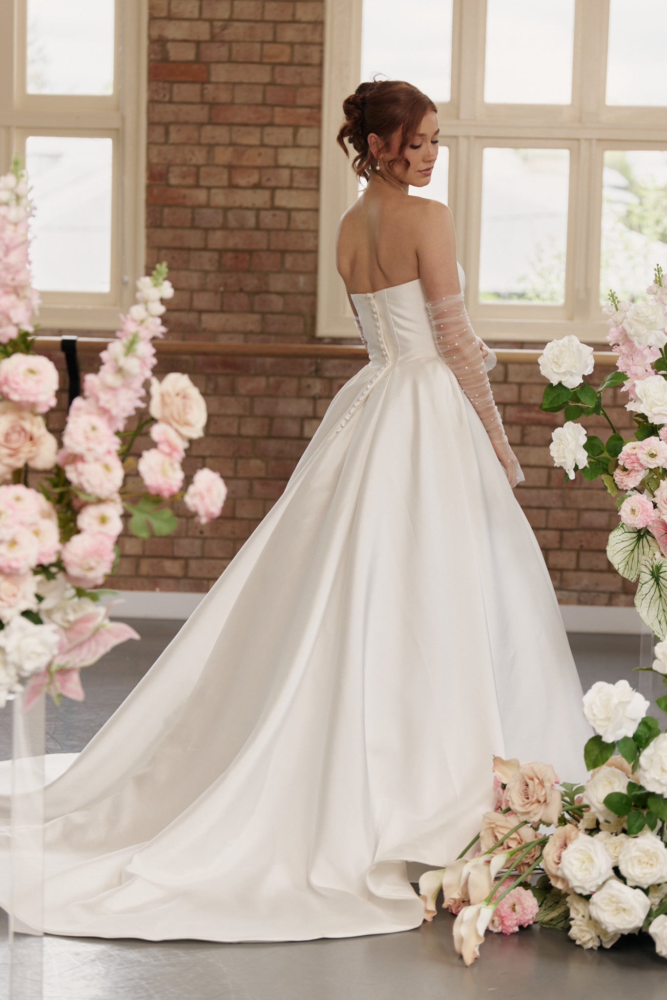 Back view of the Mackenzie bridal gown showing the structured corset bodice, basque waist detail, and flowing princess-style train.