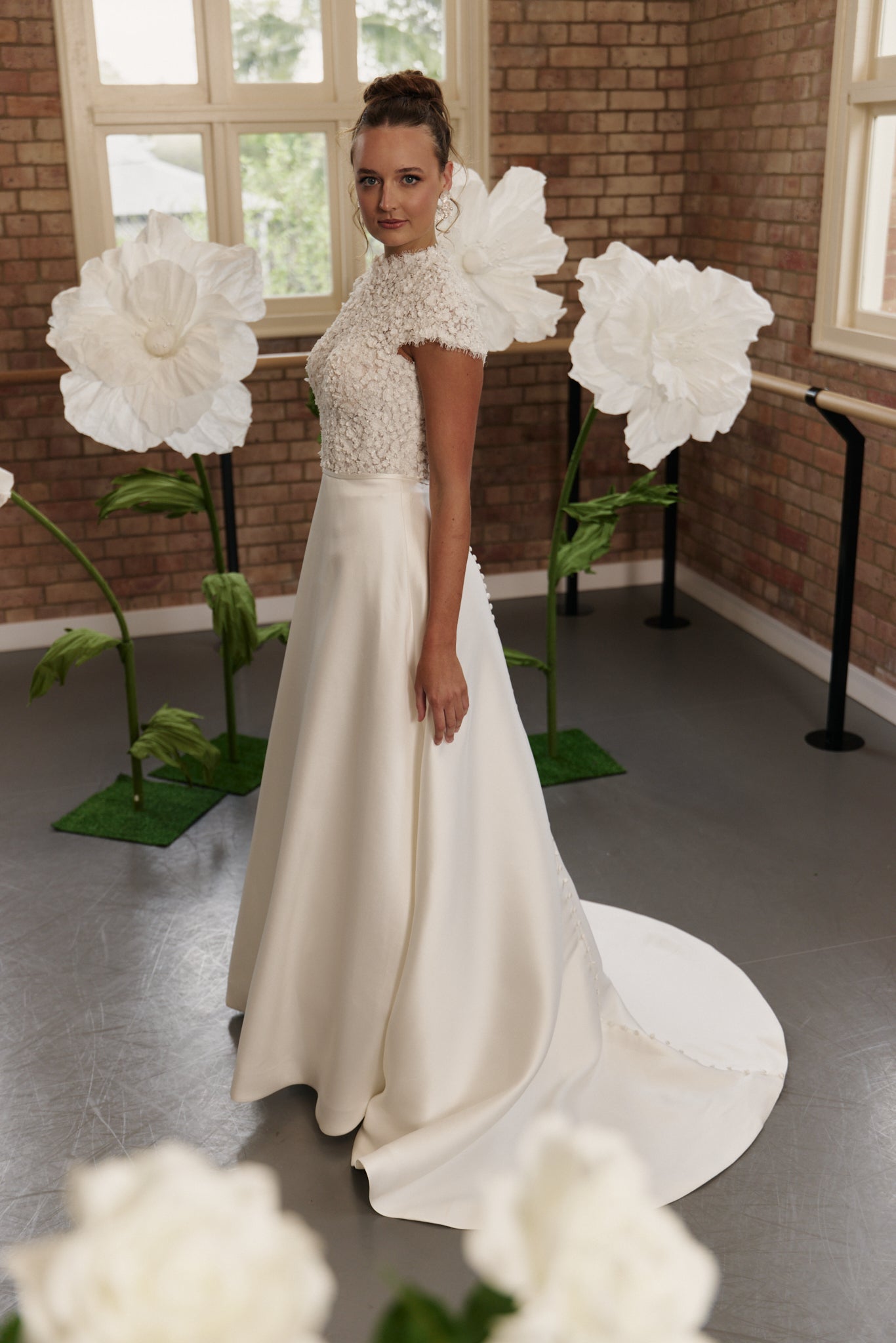 Side profile of classic wedding dress highlighting floral bodice, high neck, cap sleeves, and elegant A-line silhouette.