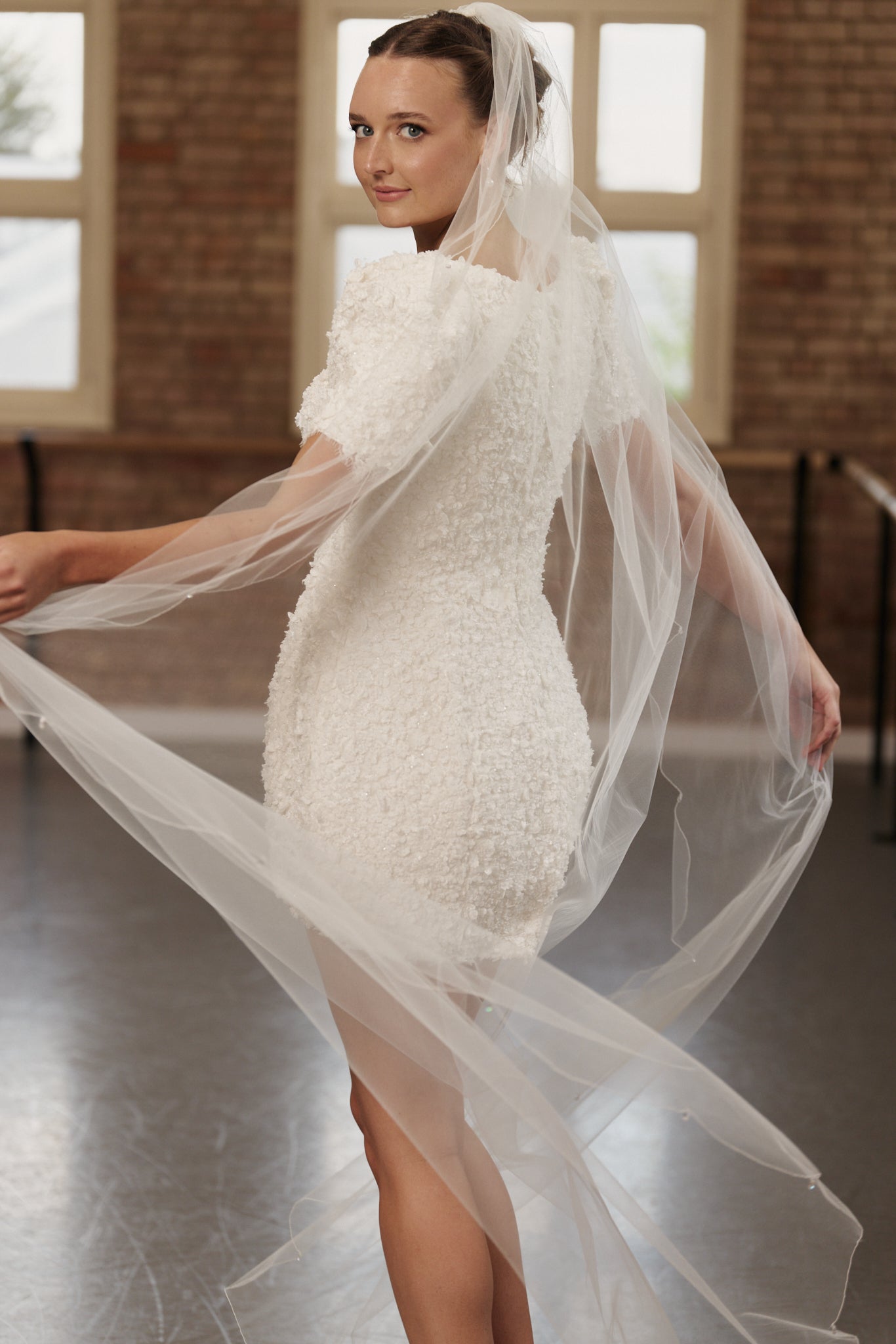 Back view of the Poppy bridal mini dress showcasing cap sleeves and delicate floral lace with veil