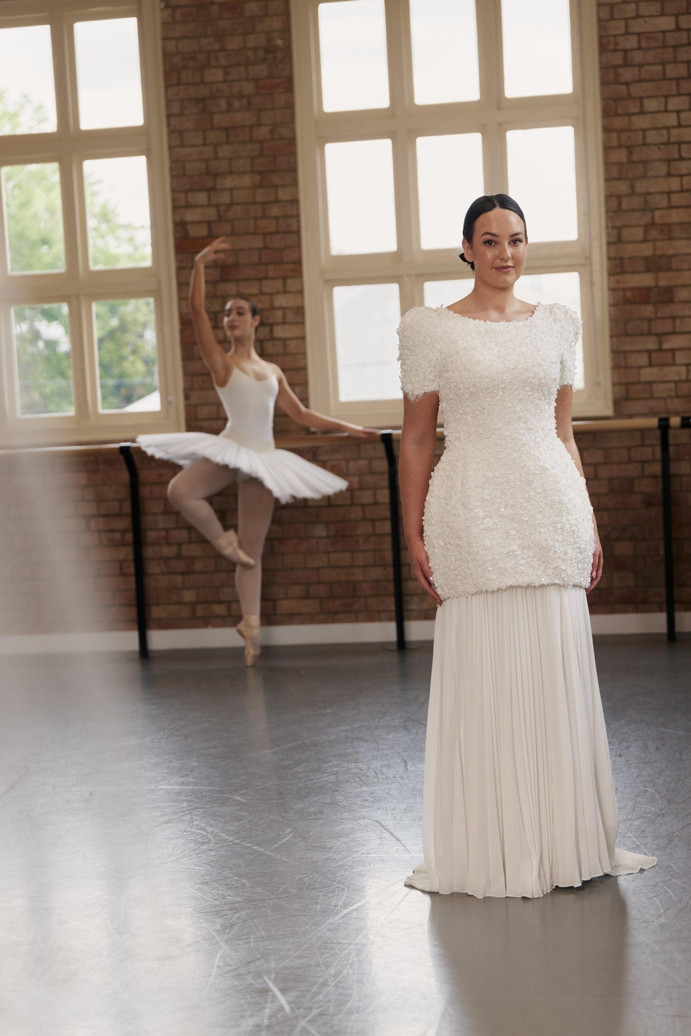 Front view of the Poppy mini wedding dress with rounded skirt, oversized cap sleeves, and textured floral lace. Pictured with sunray pleated chiffon underskirt