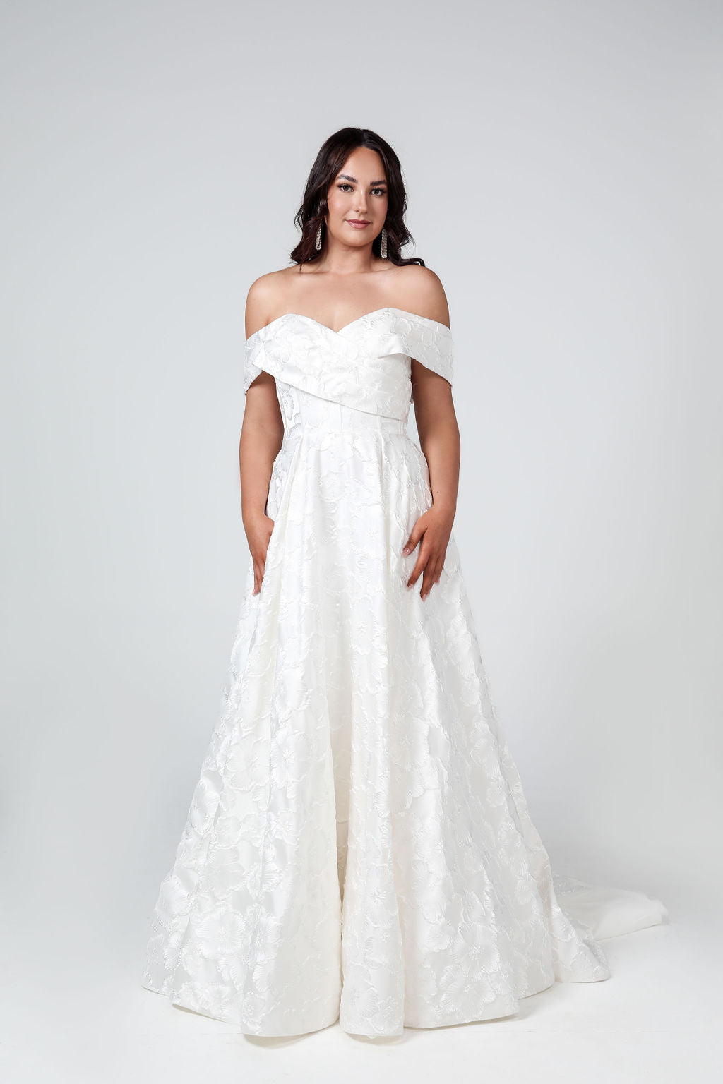Front view of the Savannah wedding gown featuring an off-shoulder wrap sleeve design with a full princess skirt in Mikado or floral jacquard.