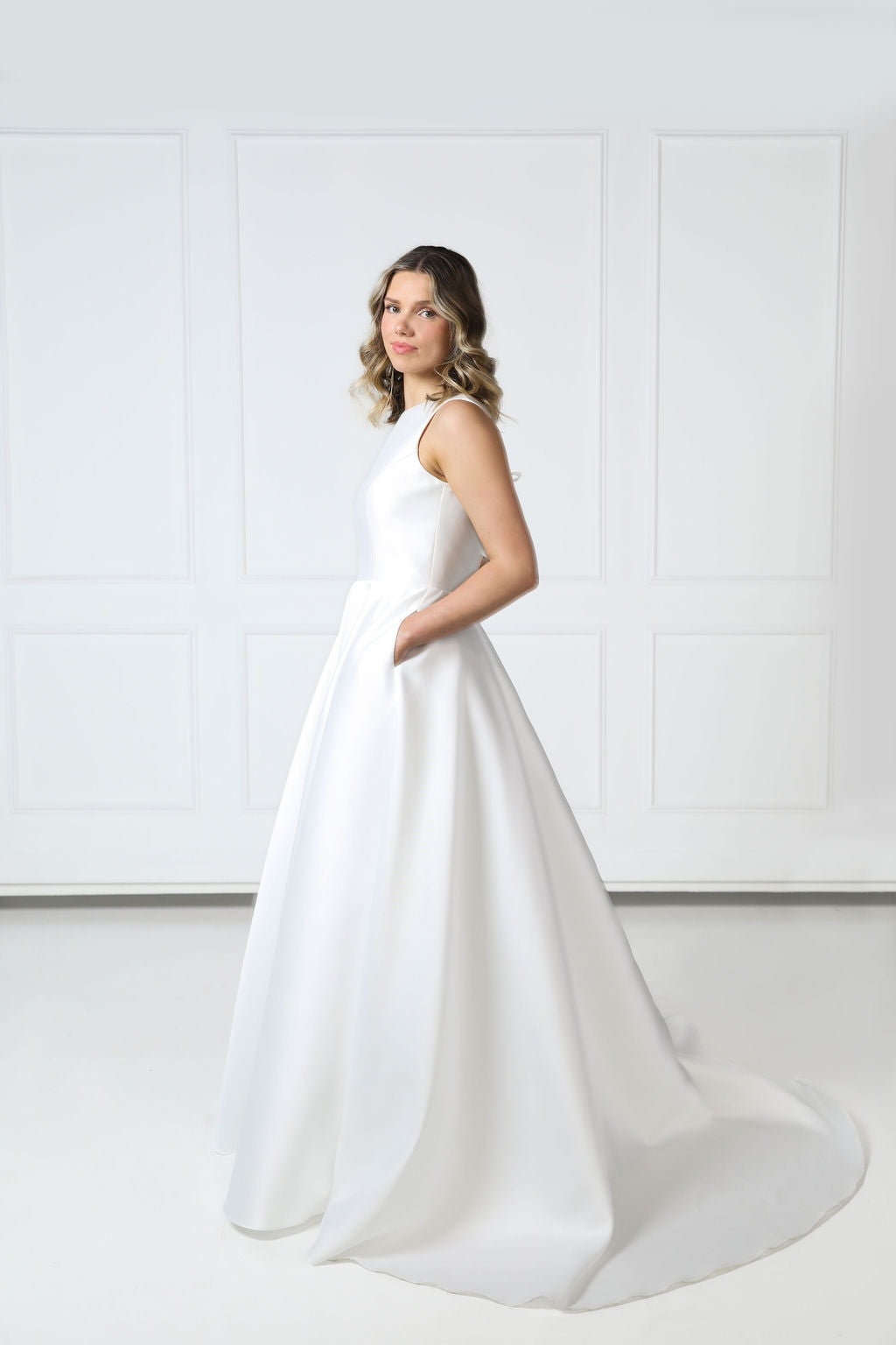 Side profile of boat-neck wedding gown showing the structured waist, flowing full skirt, and glossy Mikado finish.