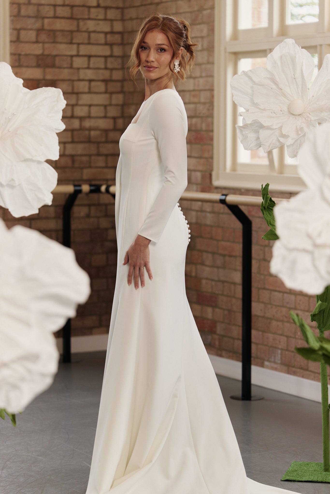 Bride wearing Charlotte long sleeve crepe sheath wedding gown with square neck and open back.
