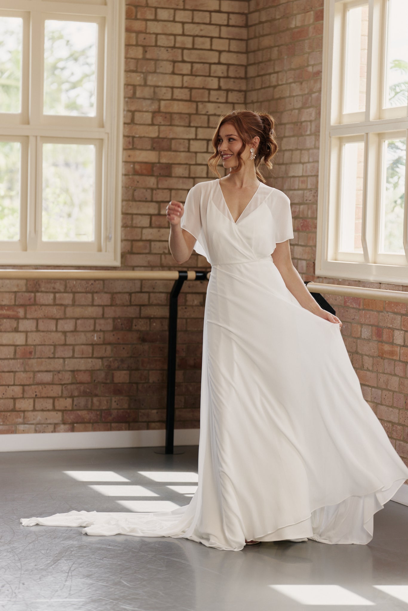 Bride wearing Clare wedding dress with flutter sleeves, V-neck crossover bodice, and flowing A-line skirt with train.