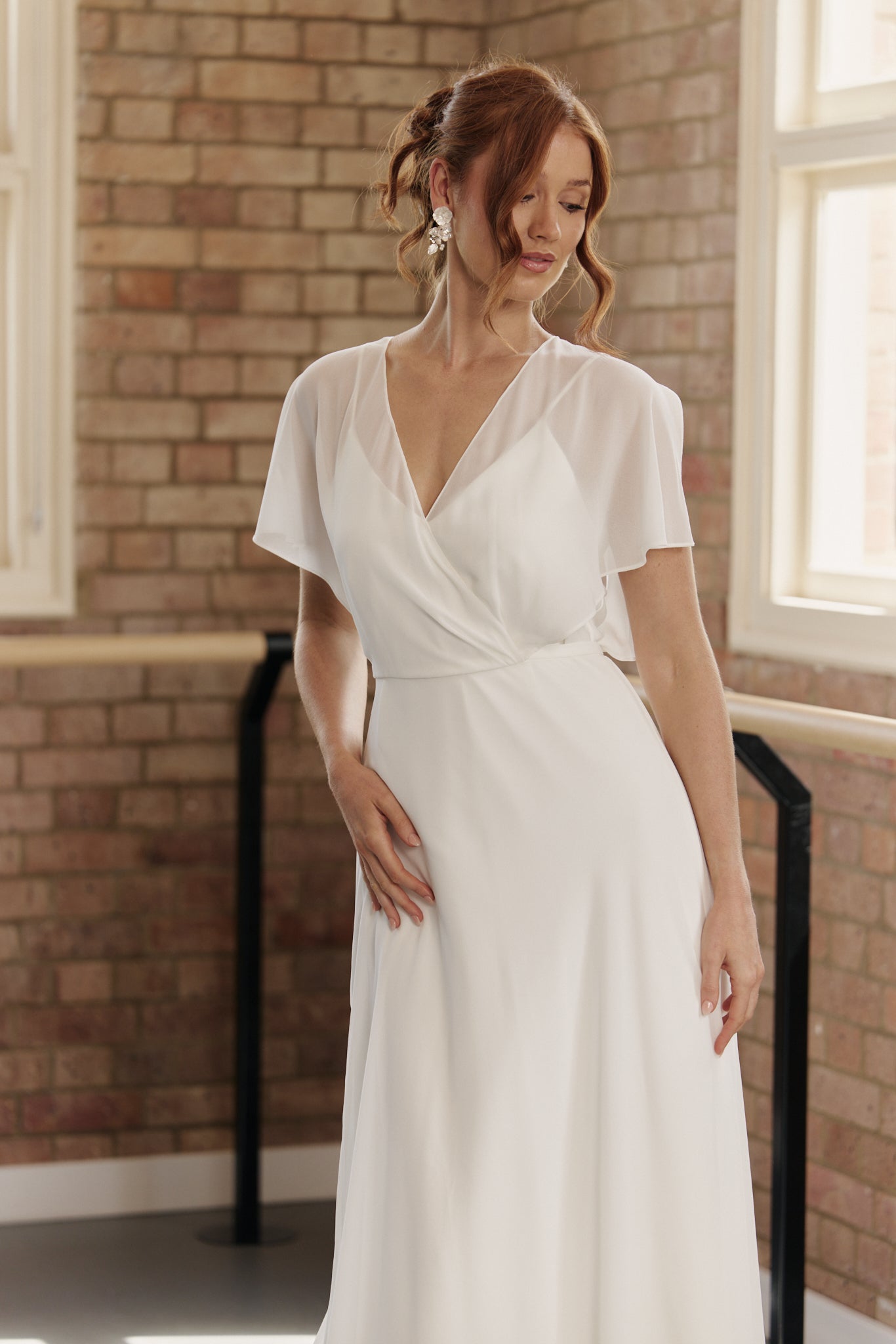 Close-up of V-neck crossover bodice and flutter sleeves on Clare wedding dress in silky fabric.