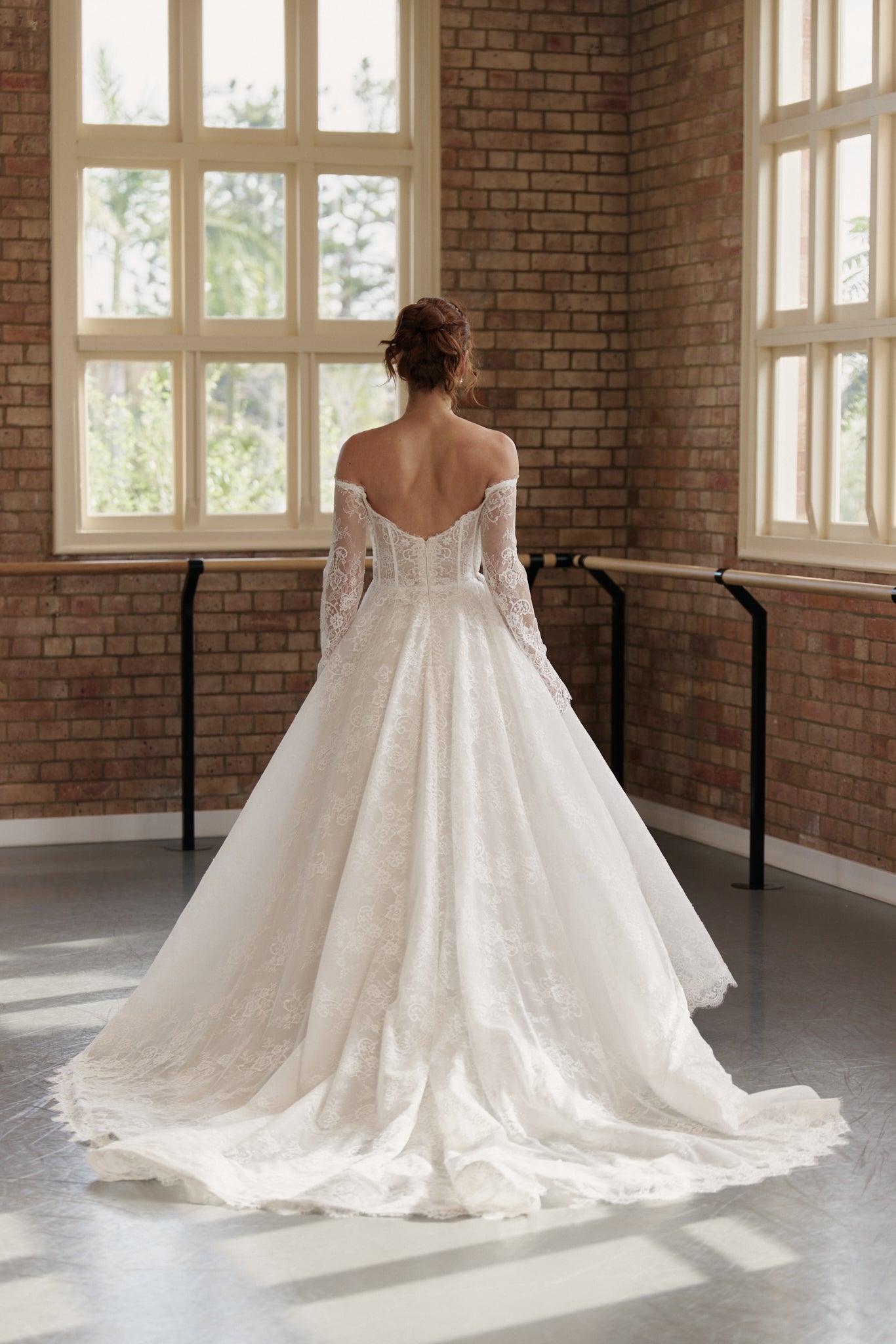 Back of Elle wedding gown showing off-shoulder long sleeves, corseted bodice, and full lace princess skirt with long train