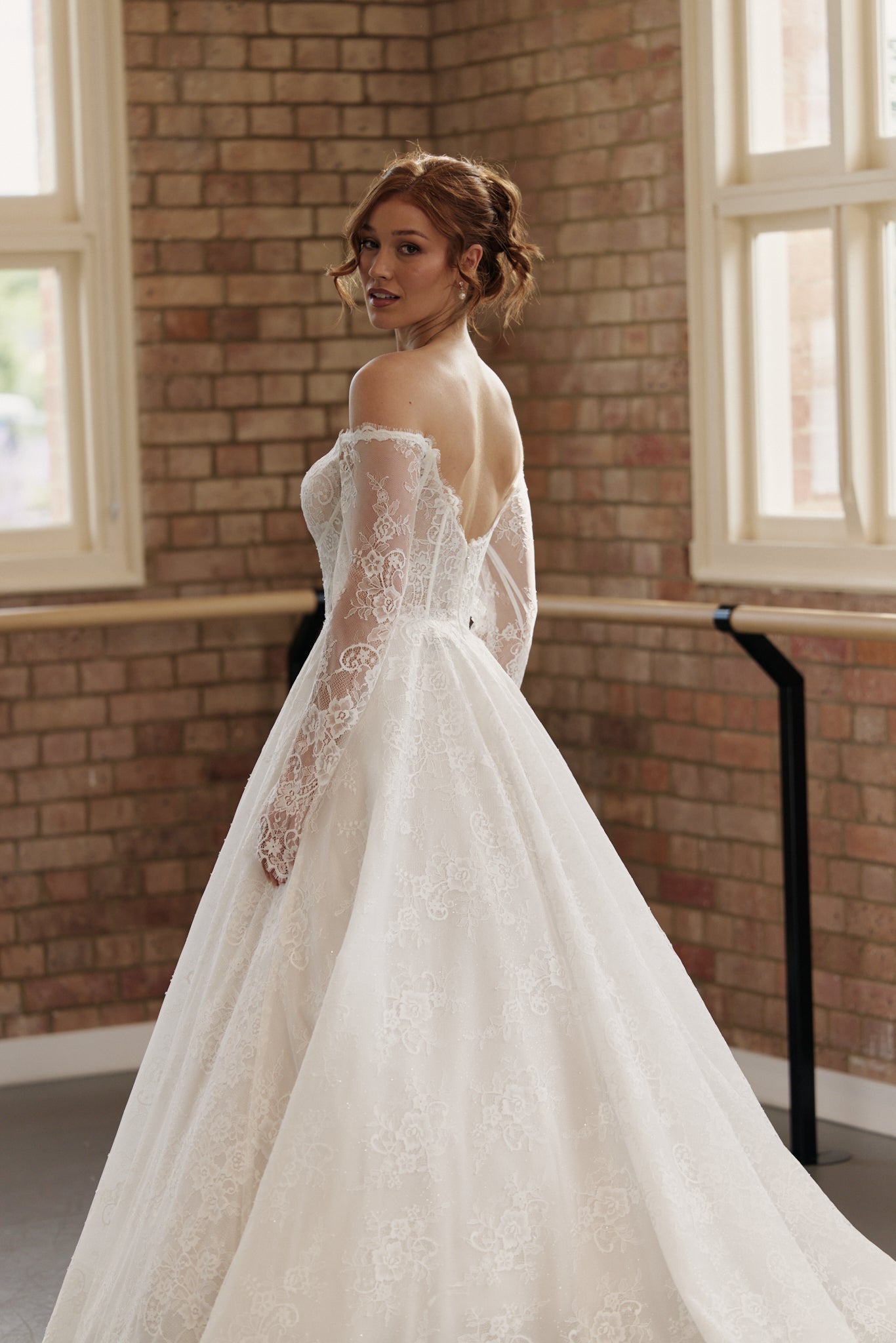 Back of Elle wedding dress showing off-shoulder long sleeves, corseted bodice, and full lace princess skirt.