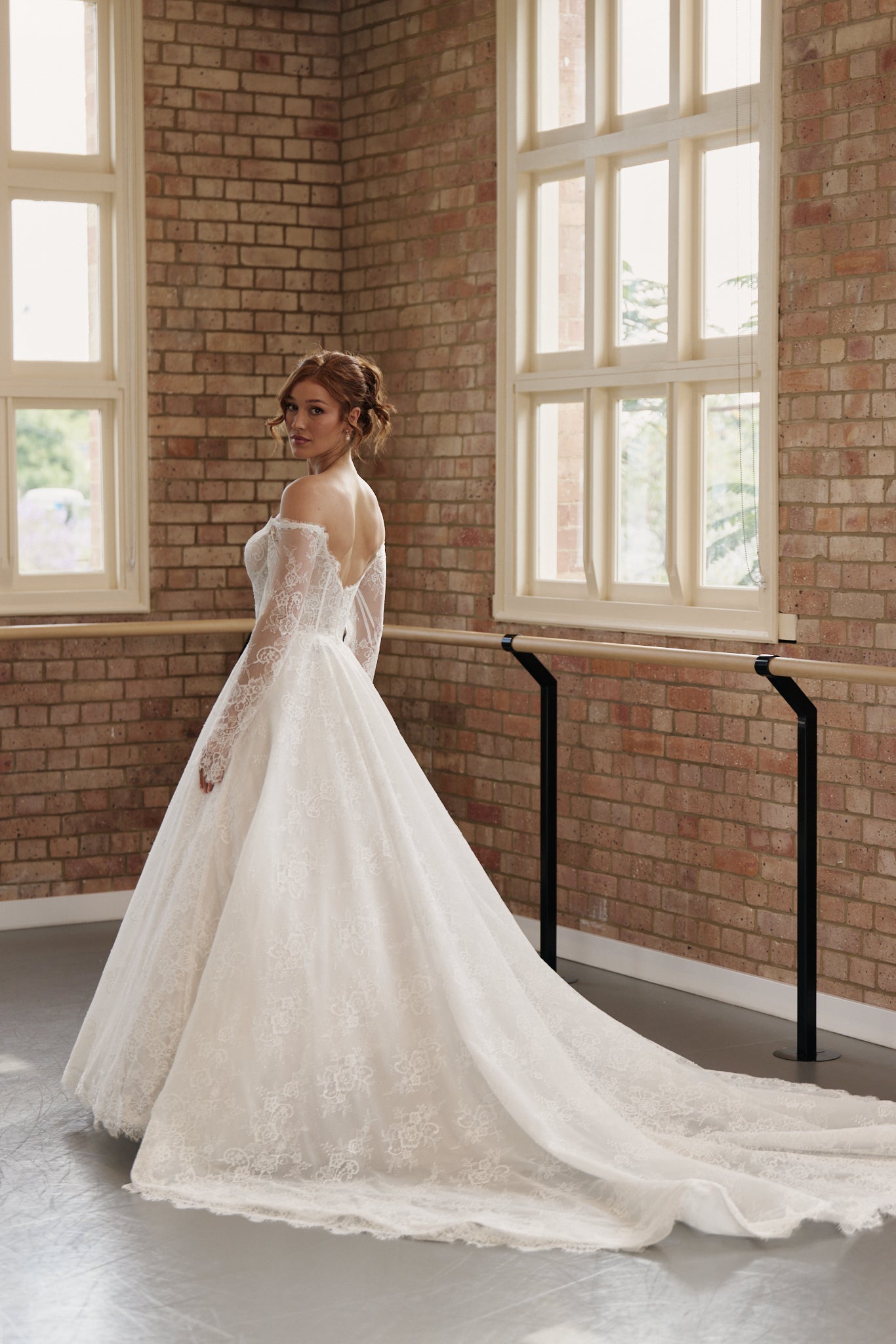 Back of Elle wedding dress showing off-shoulder long sleeves, corseted bodice, and full lace princess skirt.