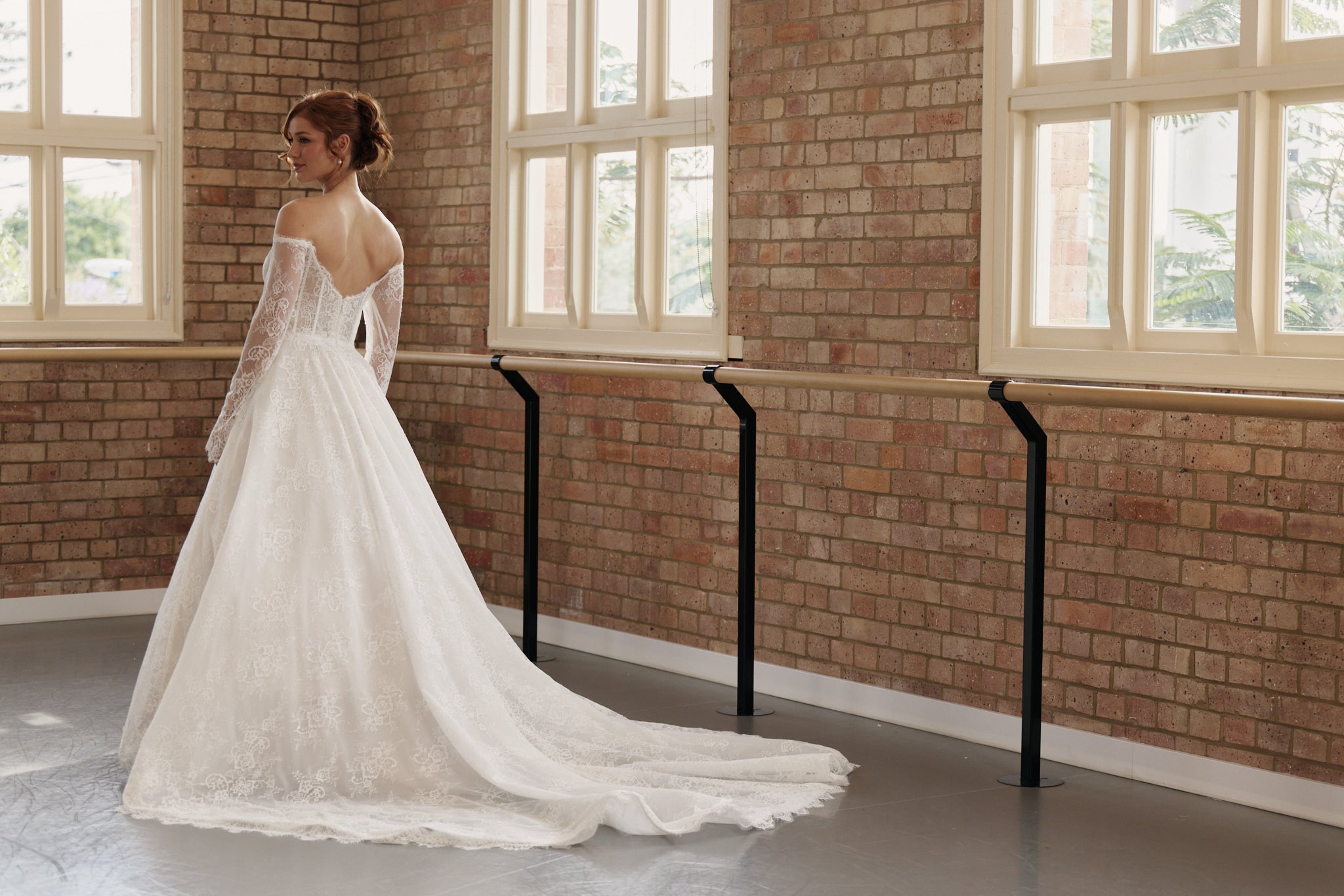 Back of Elle wedding dress showing off-shoulder long sleeves, corseted bodice, and full lace princess skirt.