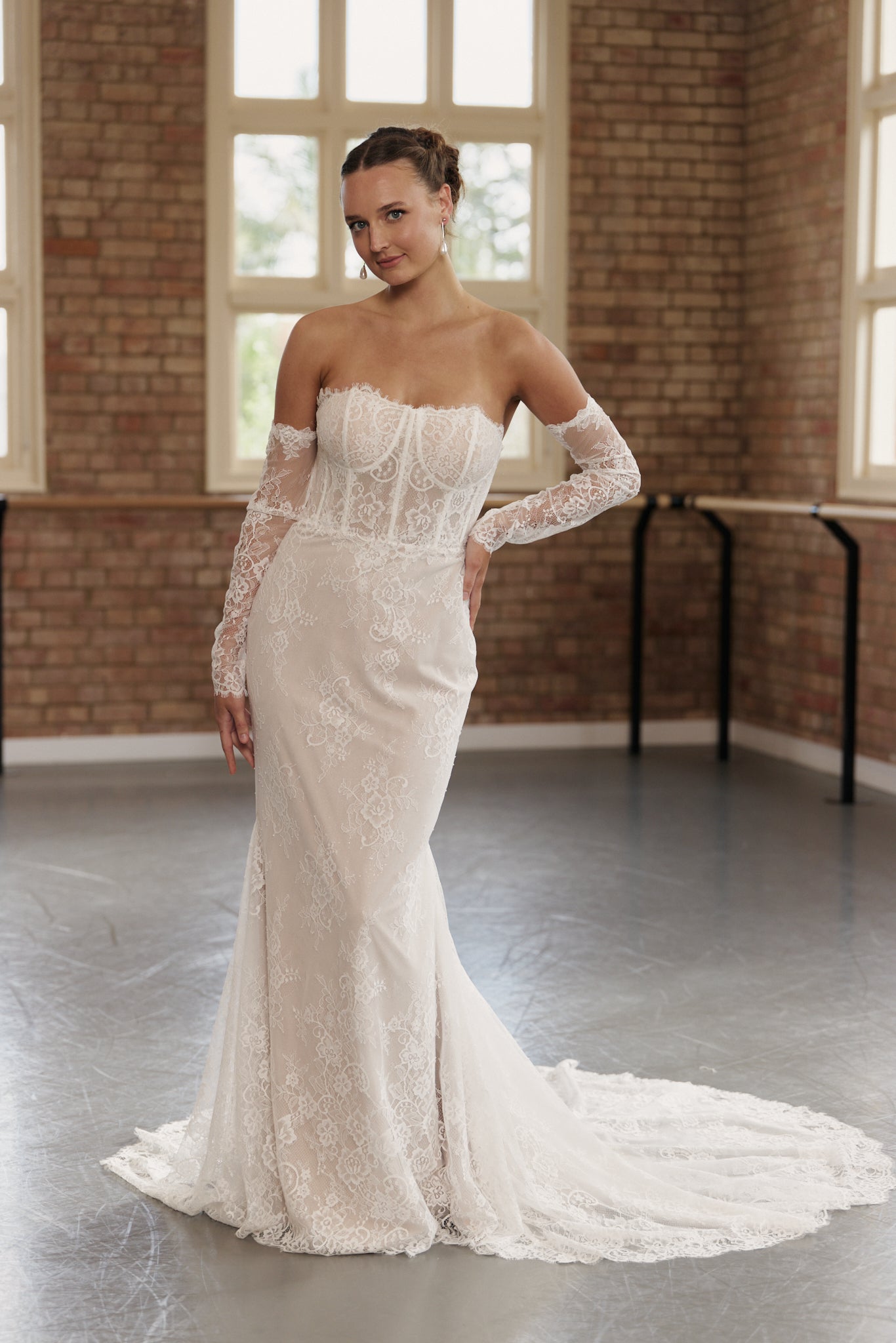 Bride wearing off-the-shoulder lace wedding dress with long lace sleeves, structured corset bodice, and mermaid silhouette.
