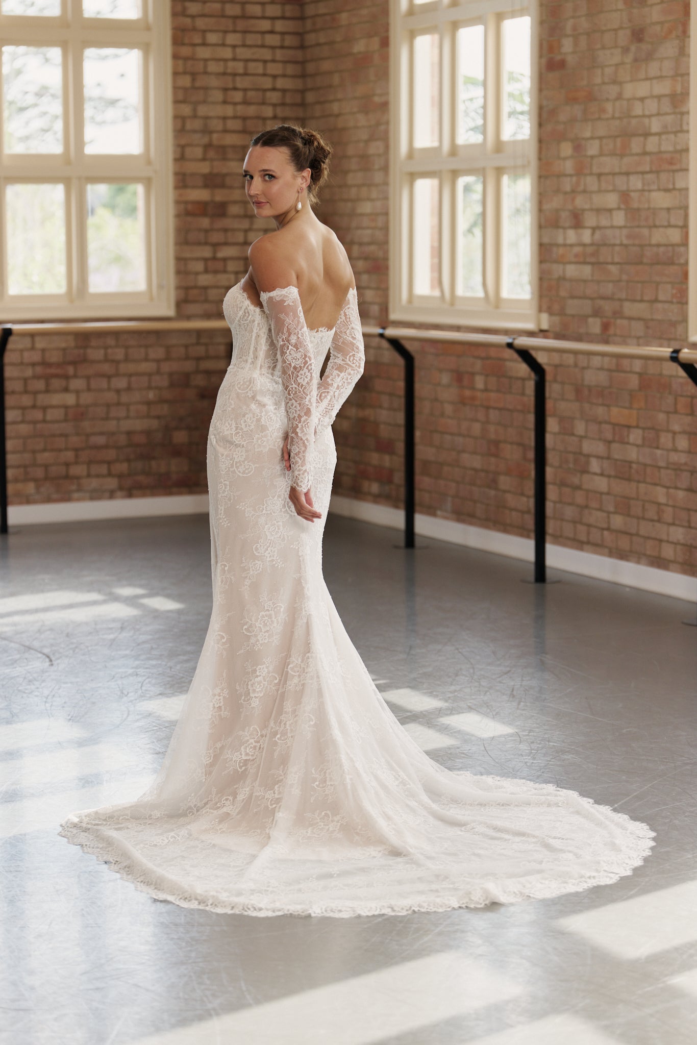 Back of off-the-shoulder lace wedding gown with clean design and figure-hugging mermaid skirt and lace sleeves.