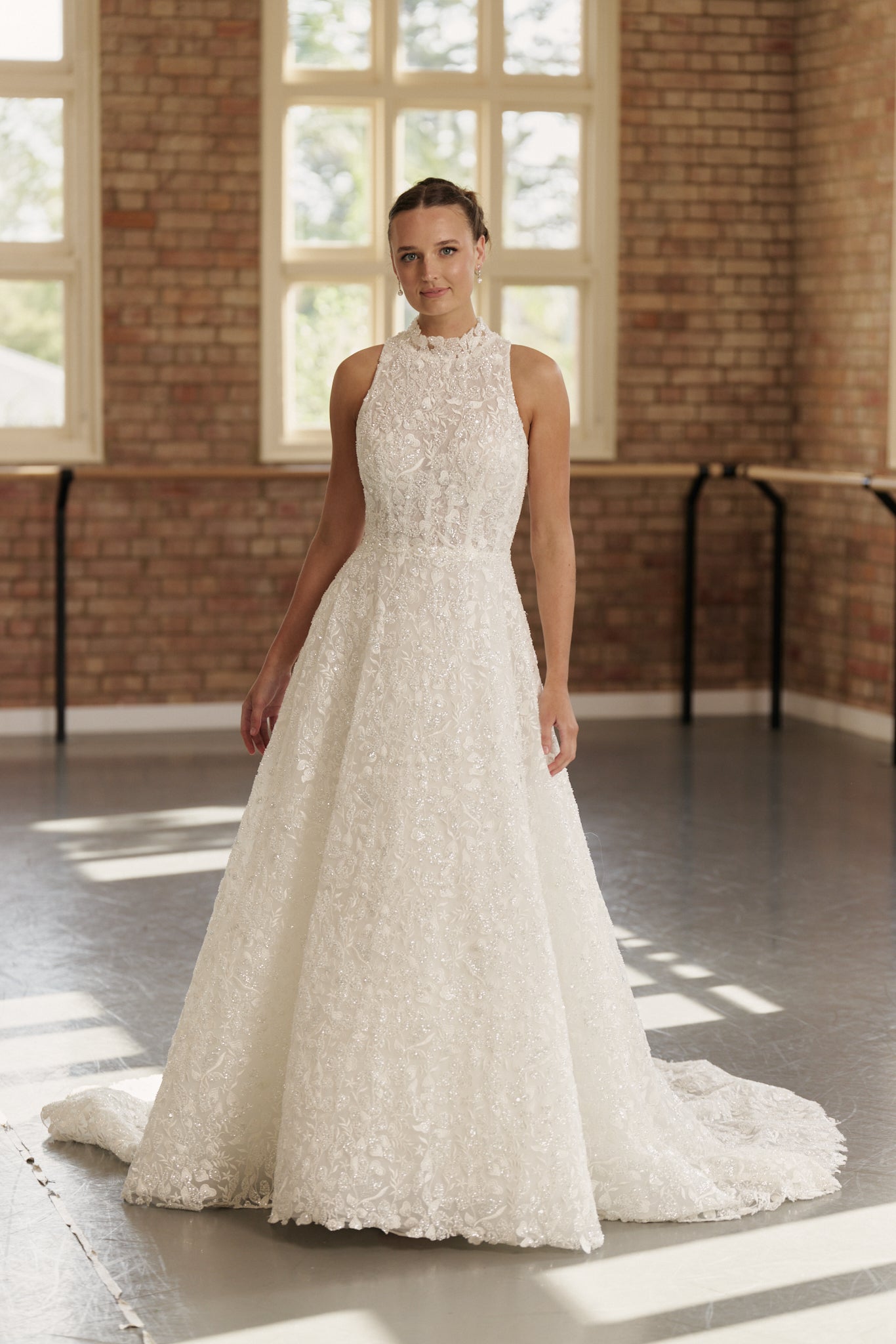 Front view of the Mia wedding dress featuring a full beaded design, high neckline, sleeveless cutaway halter silhouette, and princess-style skirt.