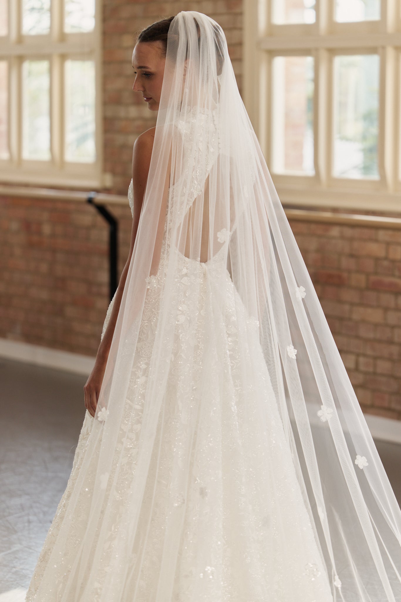 Back view of the Mia bridal gown with flower veil, showing the open back detail, shimmering beaded fabric, and voluminous princess-style skirt.