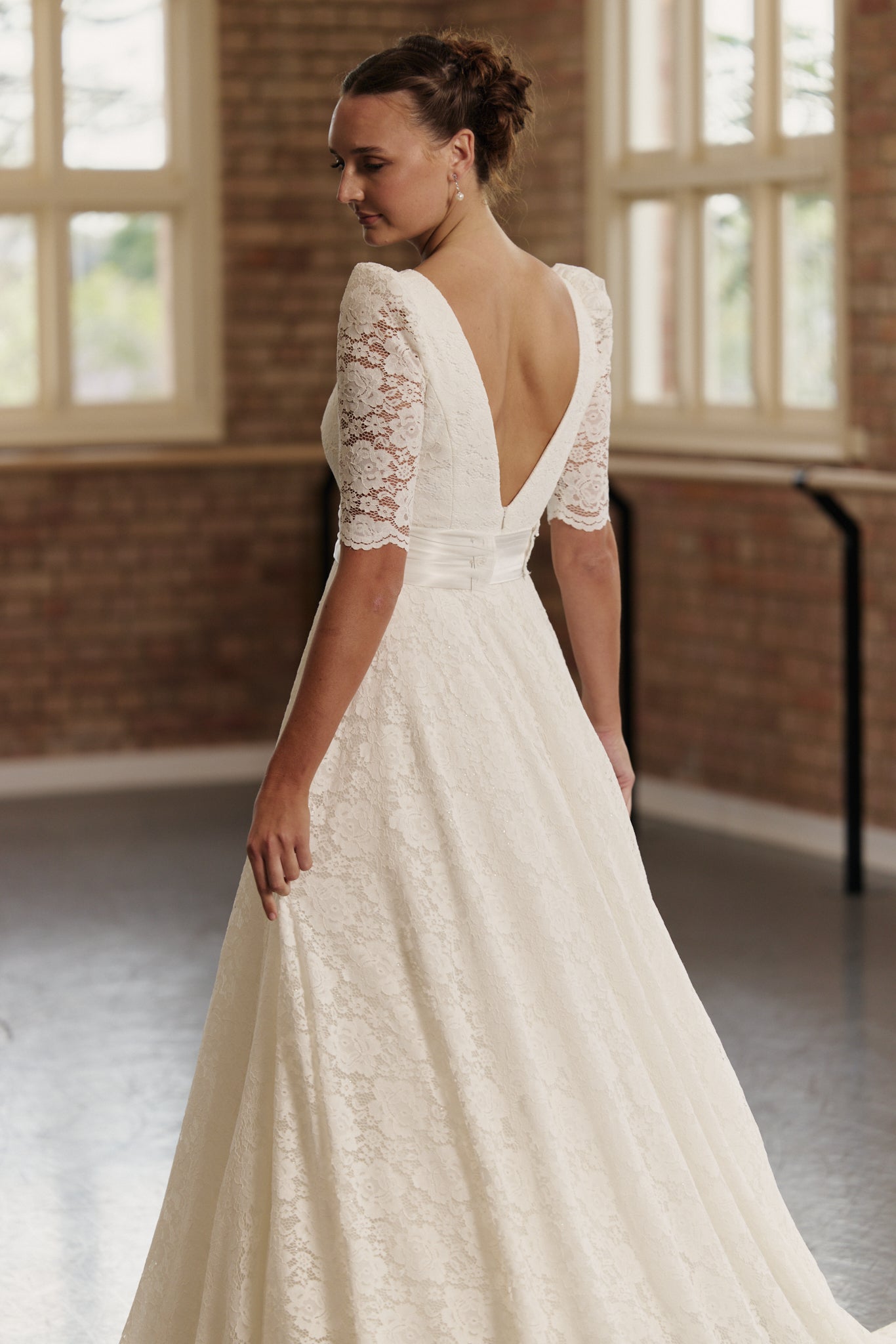 Back view of the Roma bridal gown showcasing the delicate lace, cinched silk waistband, deep V back and graceful full A-line skirt.