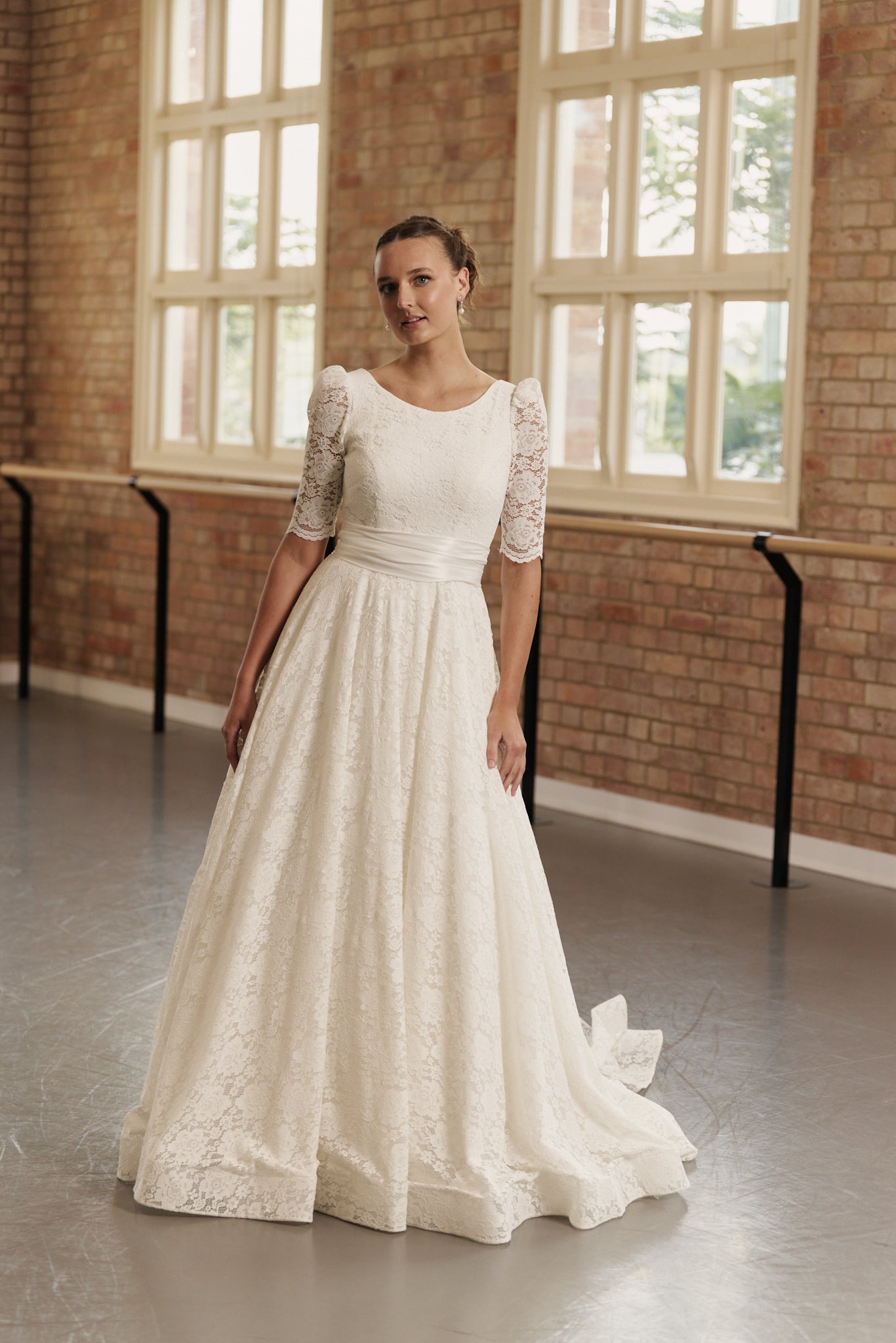 Front view of the Roma full lace wedding gown with soft boat neckline, ruched silk waistband, and flowing A-line skirt.