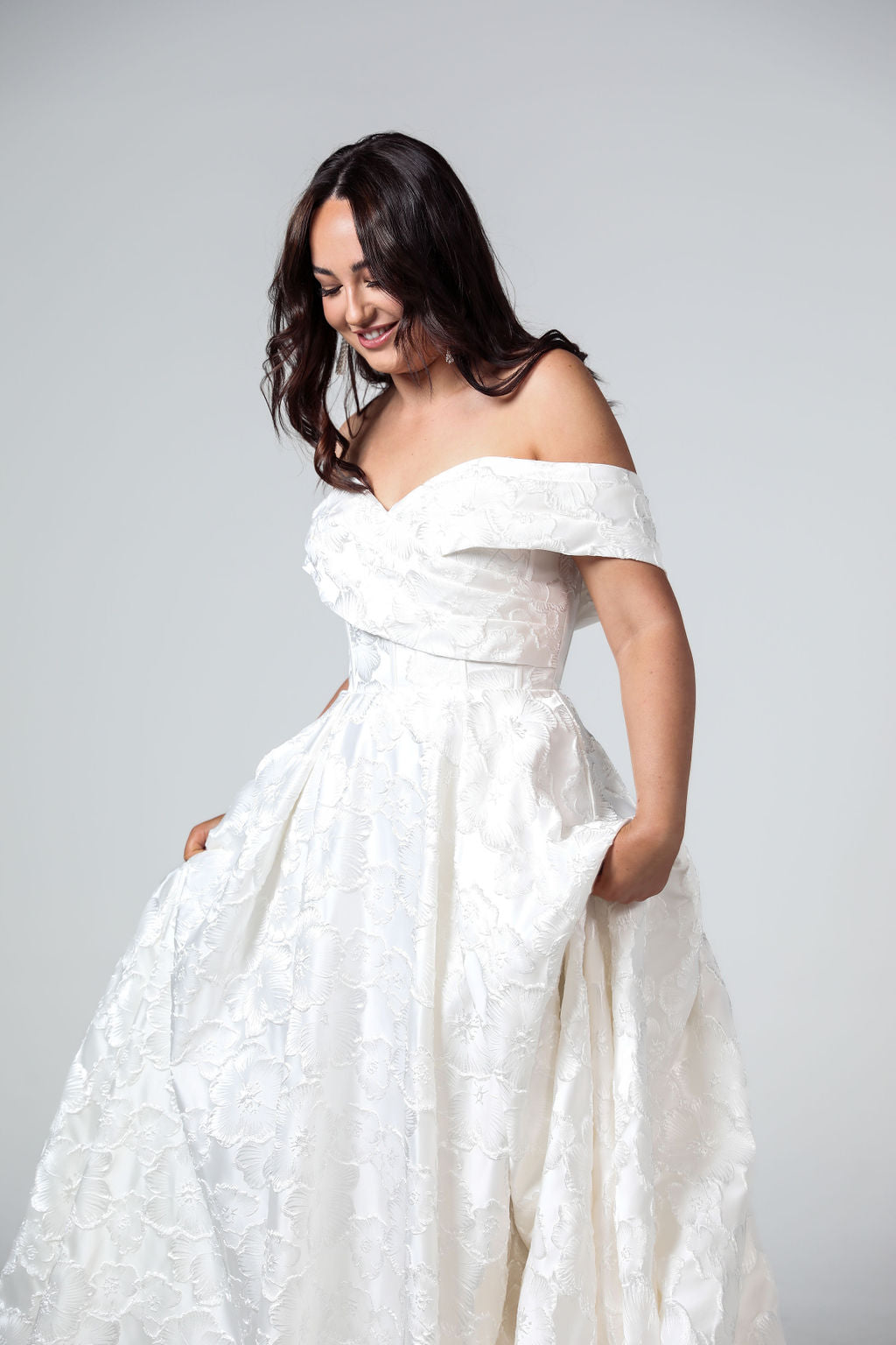 Side profile of the Savannah bridal gown highlighting the off-shoulder wrap sleeves, fitted bodice, and voluminous princess silhouette.