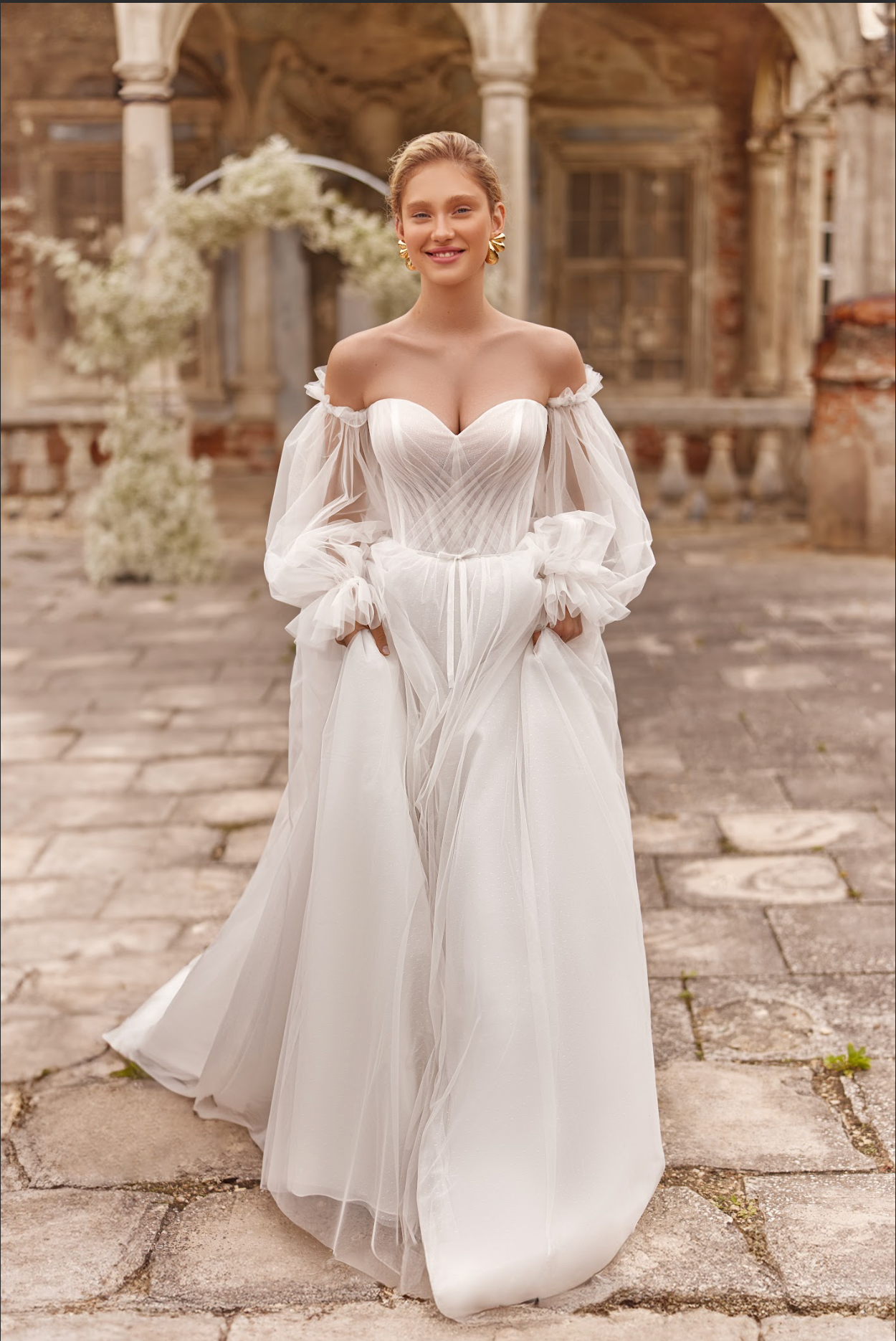 Vesta Wedding Gown, corset bodice with pleated ruching across bodice, flowy tulle skirt, detachable long sleeves, sweetheart neckline, strapless, delicate bow at waist.